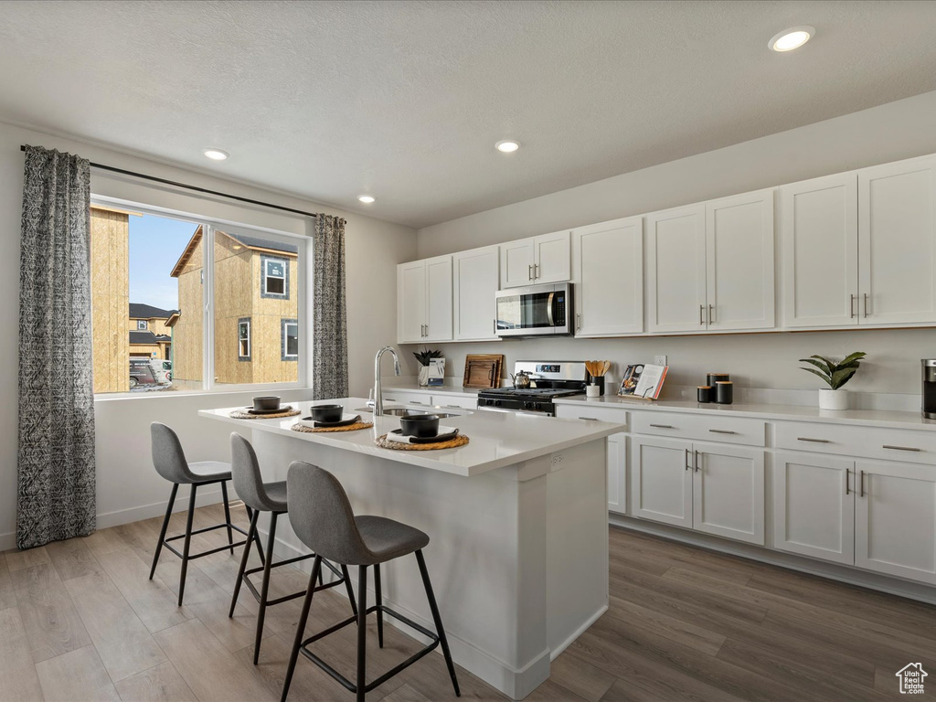 Kitchen featuring a breakfast bar, a kitchen island with sink, a sink, wood finished floors, and appliances with stainless steel finishes