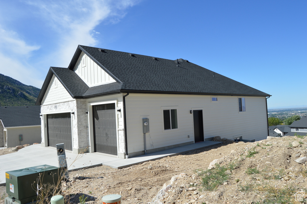 Rear view of property with an attached garage, board and batten siding, driveway, and roof with shingles