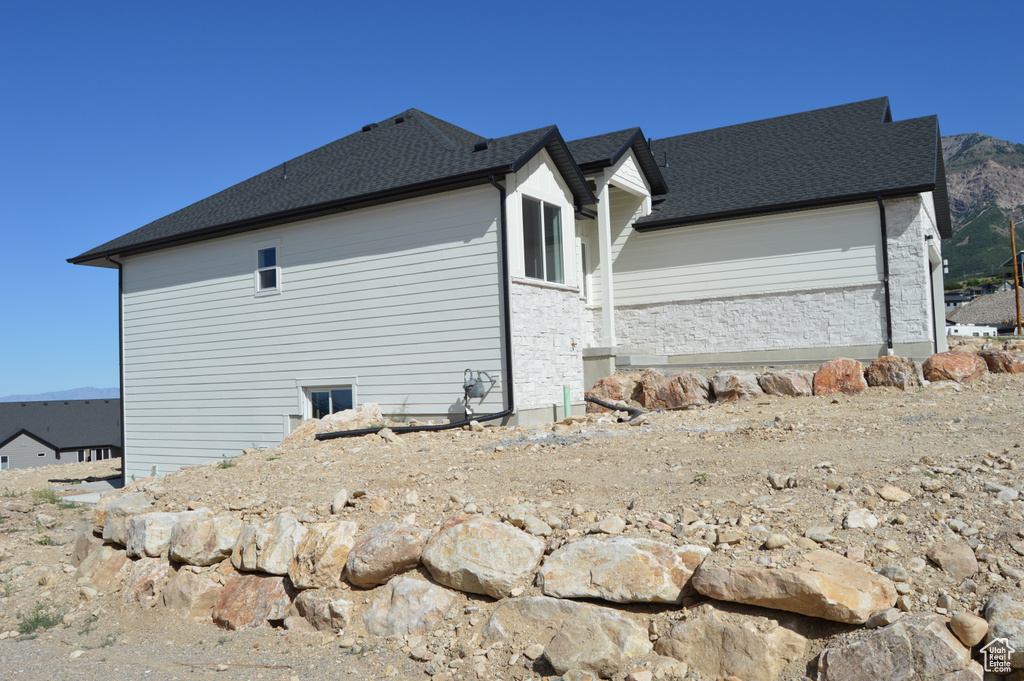 View of side of property featuring a shingled roof and stone siding