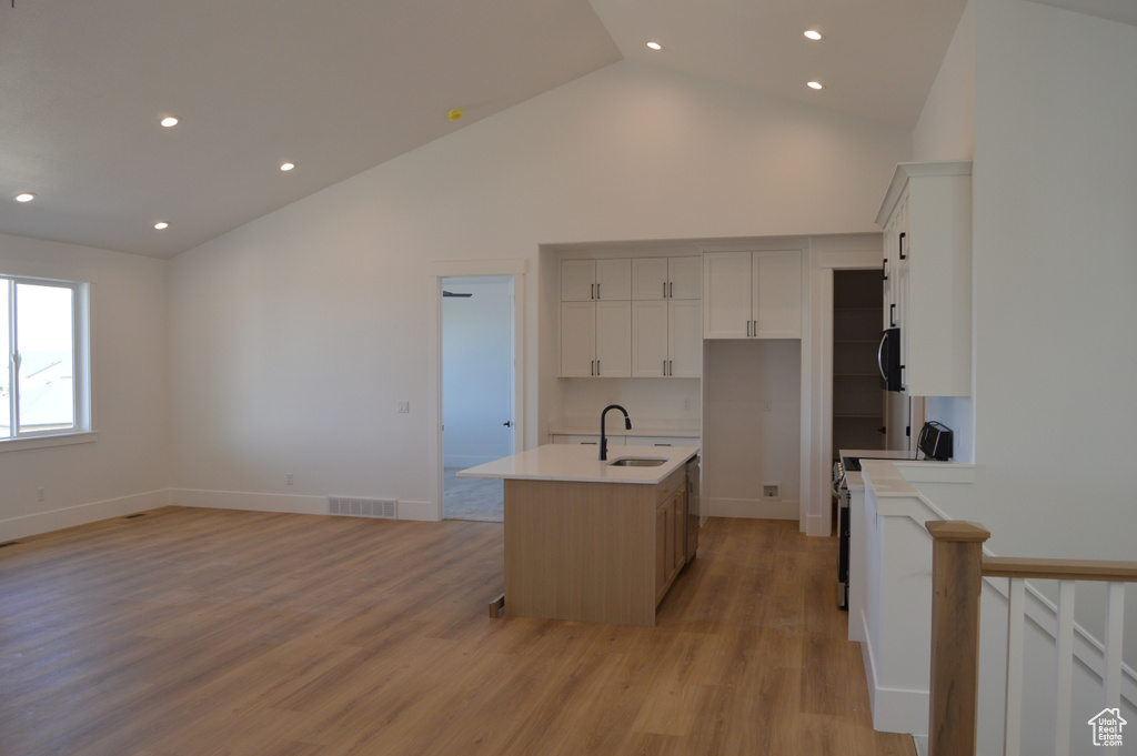 Kitchen with high vaulted ceiling, light countertops, light wood finished floors, a center island with sink, and recessed lighting