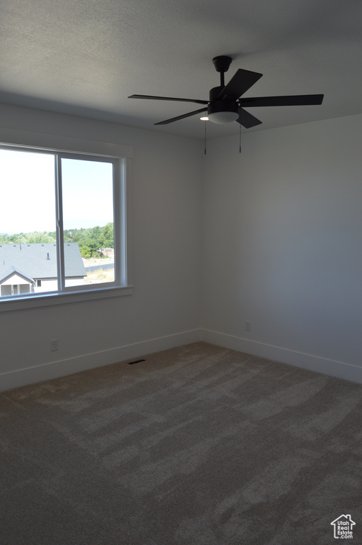 Carpeted spare room featuring ceiling fan and baseboards