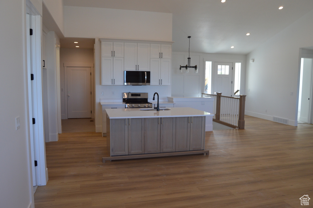 Kitchen featuring appliances with stainless steel finishes, light wood finished floors, white cabinetry, an island with sink, and light countertops