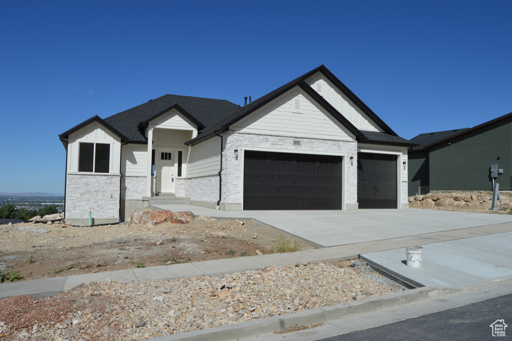 Modern farmhouse with an attached garage, driveway, stone siding, and board and batten siding