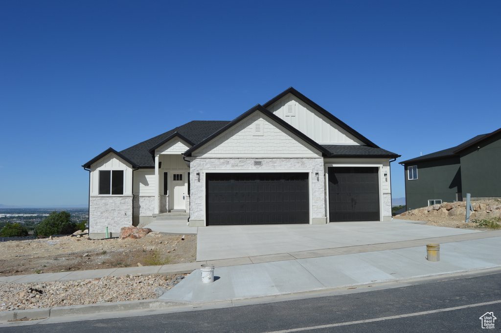 Modern farmhouse with an attached garage, stone siding, board and batten siding, and driveway
