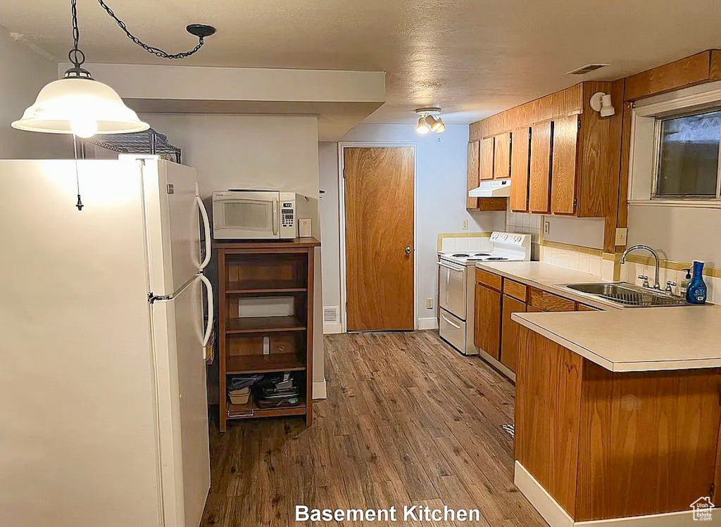 Kitchen featuring light countertops, white appliances, brown cabinets, under cabinet range hood, and a sink