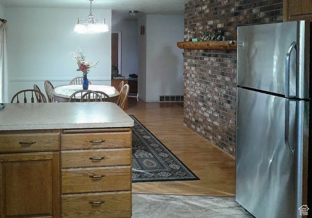 Kitchen featuring visible vents, brown cabinets, wood finished floors, a notable chandelier, and freestanding refrigerator