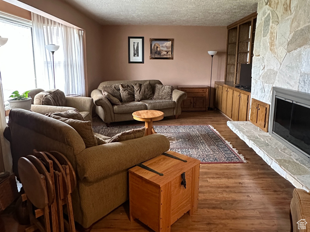 Living area with a stone fireplace, wood finished floors, and a textured ceiling