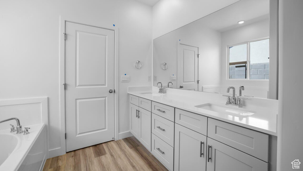 Full bathroom featuring double vanity, a sink, a garden tub, and wood finished floors