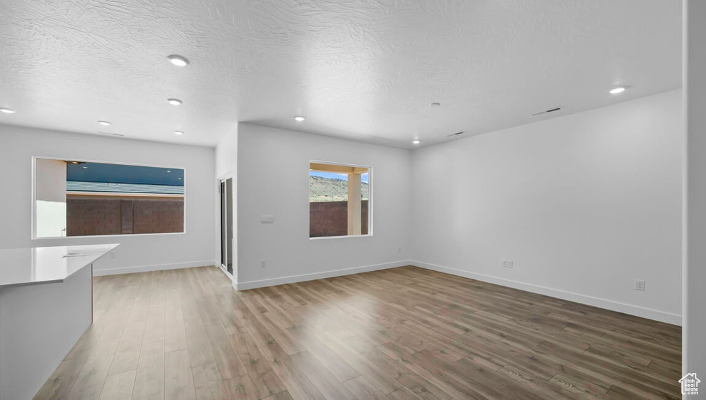 Unfurnished living room featuring recessed lighting, a textured ceiling, baseboards, and wood finished floors