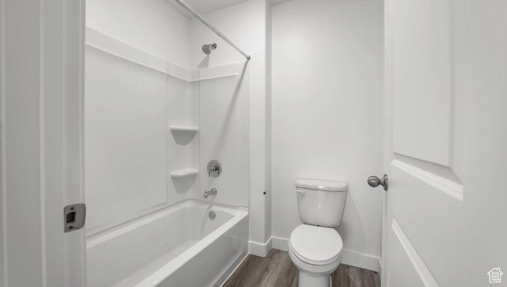Bathroom featuring baseboards, shower / tub combination, wood finished floors, and toilet