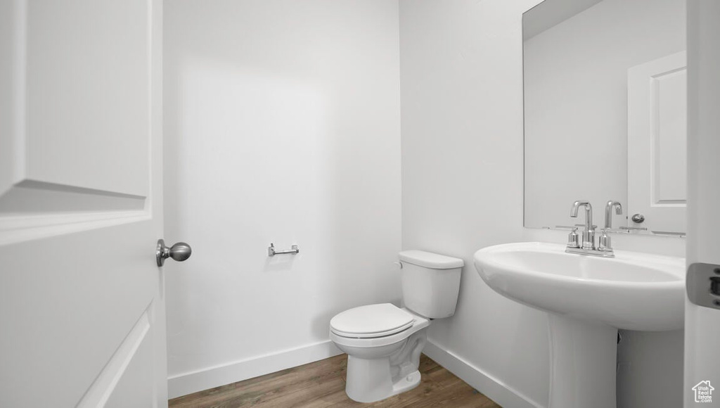 Half bath featuring baseboards, toilet, and wood finished floors