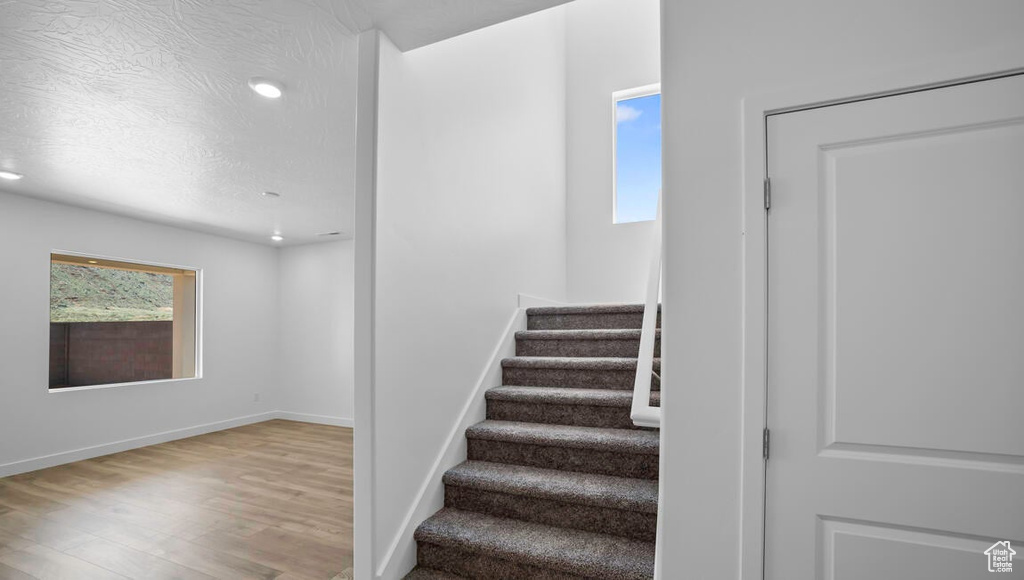 Stairs featuring baseboards, a textured ceiling, wood finished floors, and recessed lighting