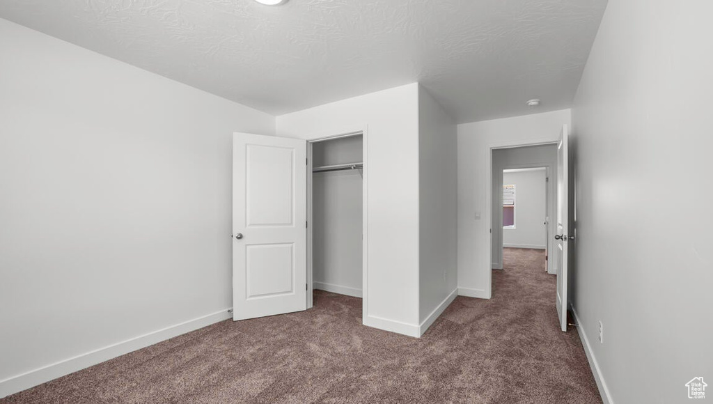 Unfurnished bedroom with baseboards, a closet, dark carpet, and a textured ceiling