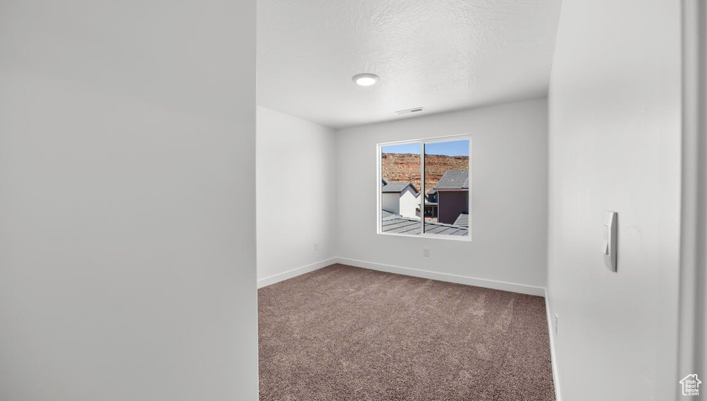 Spare room featuring baseboards, carpet floors, a textured ceiling, and visible vents
