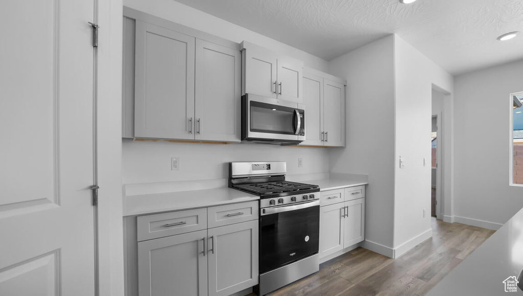 Kitchen with light countertops, wood finished floors, a textured ceiling, stainless steel appliances, and baseboards