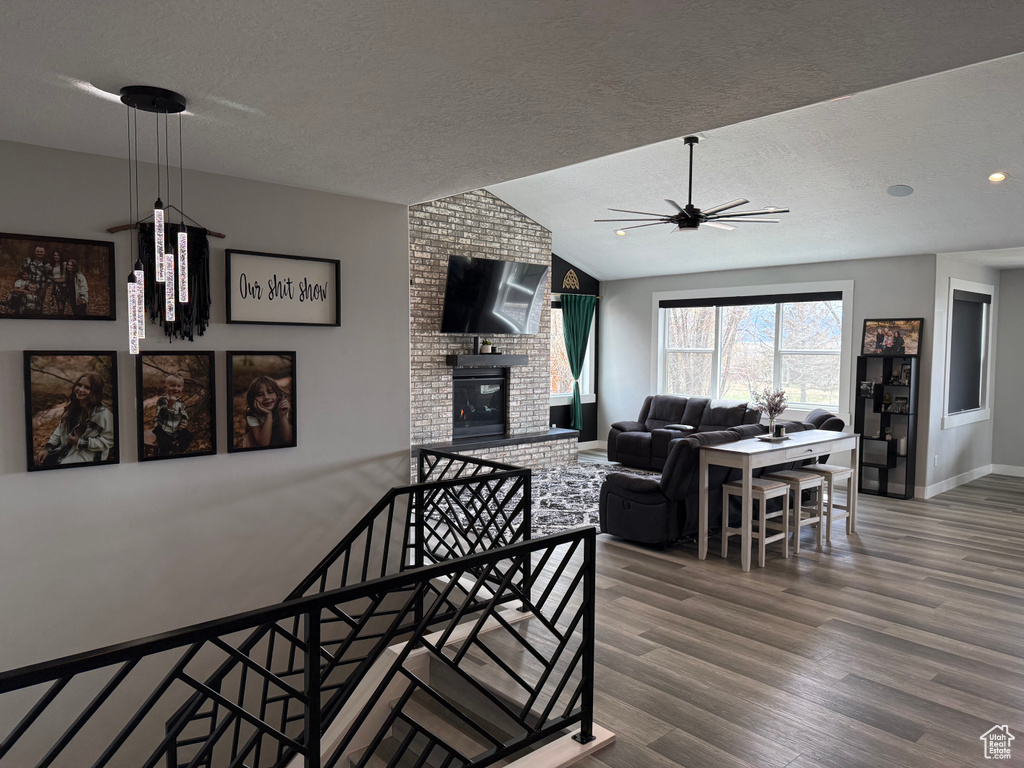 Living room featuring lofted ceiling, a textured ceiling, a ceiling fan, a fireplace, and wood finished floors