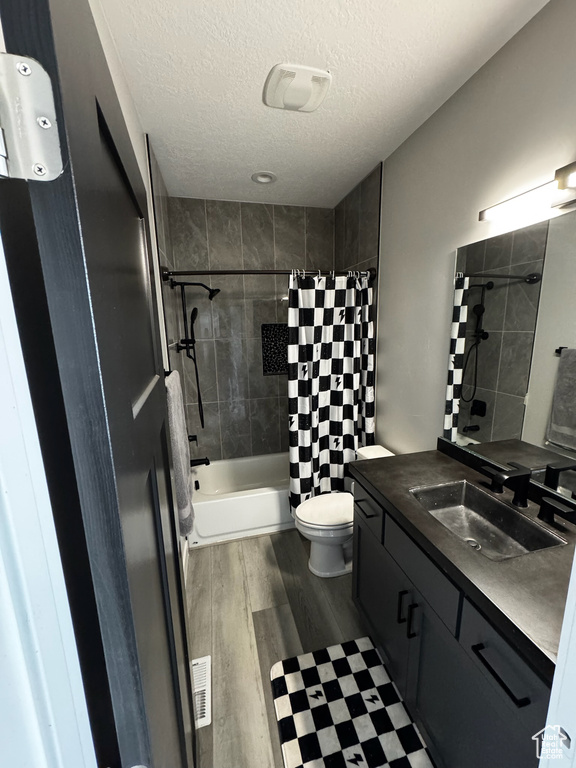 Full bathroom with vanity, shower / tub combo with curtain, wood finished floors, a textured ceiling, and toilet