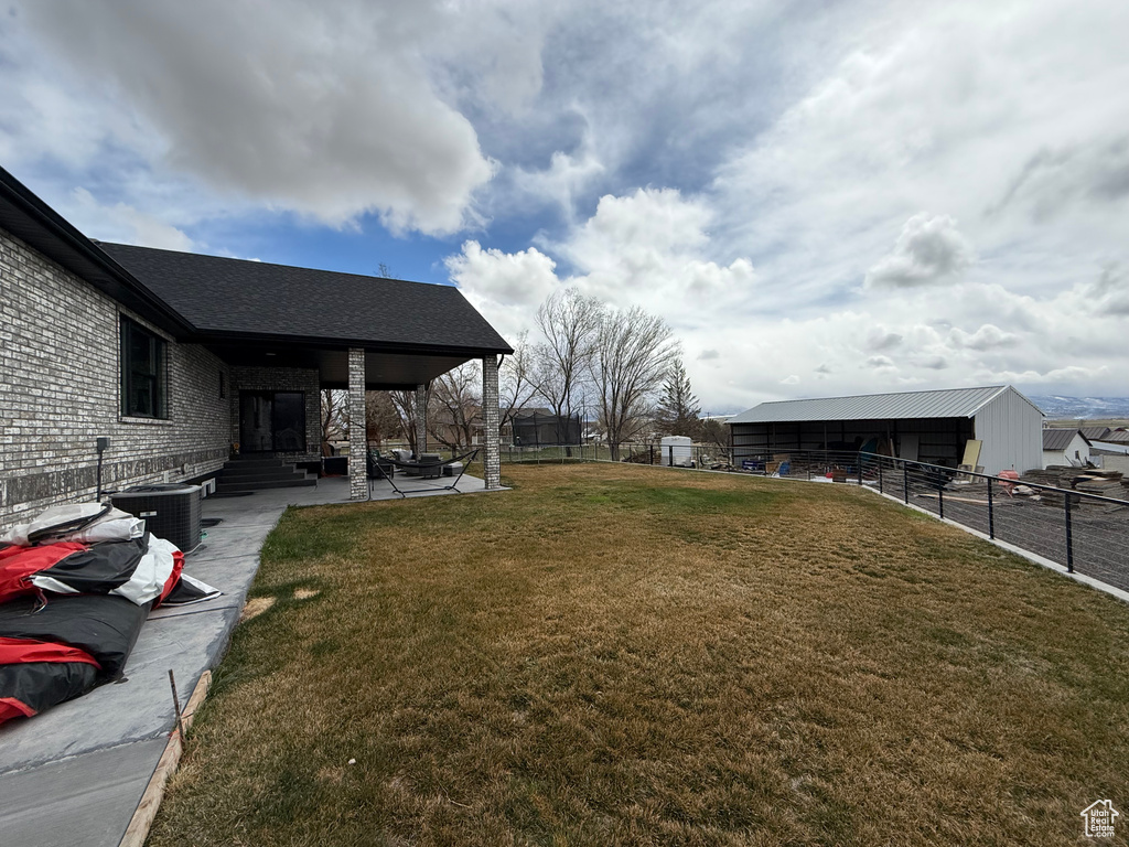 View of yard with cooling unit, an outdoor structure, fence, and a patio area