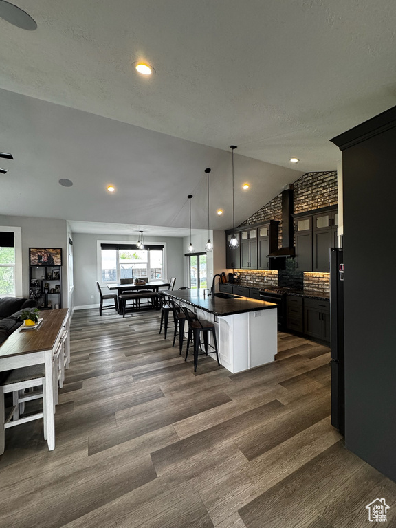 Kitchen featuring dark countertops, a sink, wall chimney range hood, plenty of natural light, and lofted ceiling