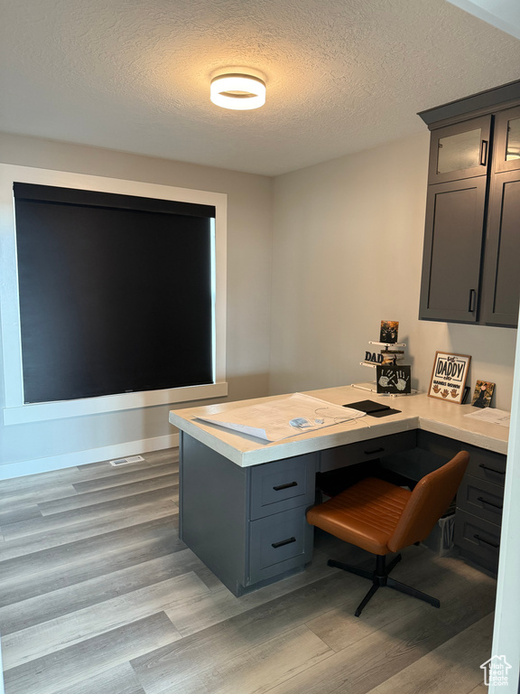 Office with built in desk, a textured ceiling, baseboards, and light wood-type flooring