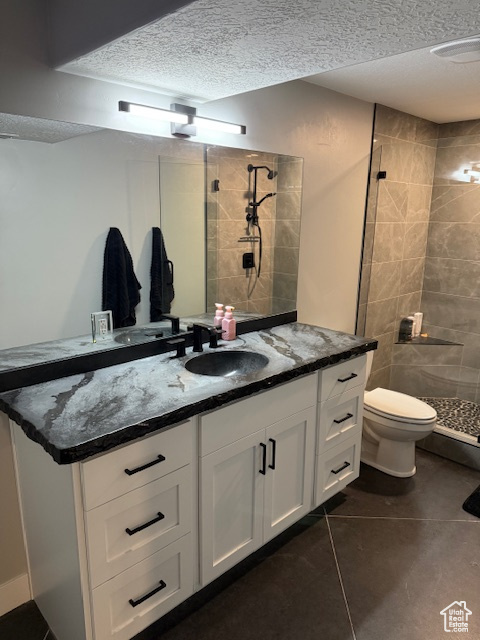 Bathroom featuring a stall shower, toilet, vanity, a textured ceiling, and tile patterned flooring