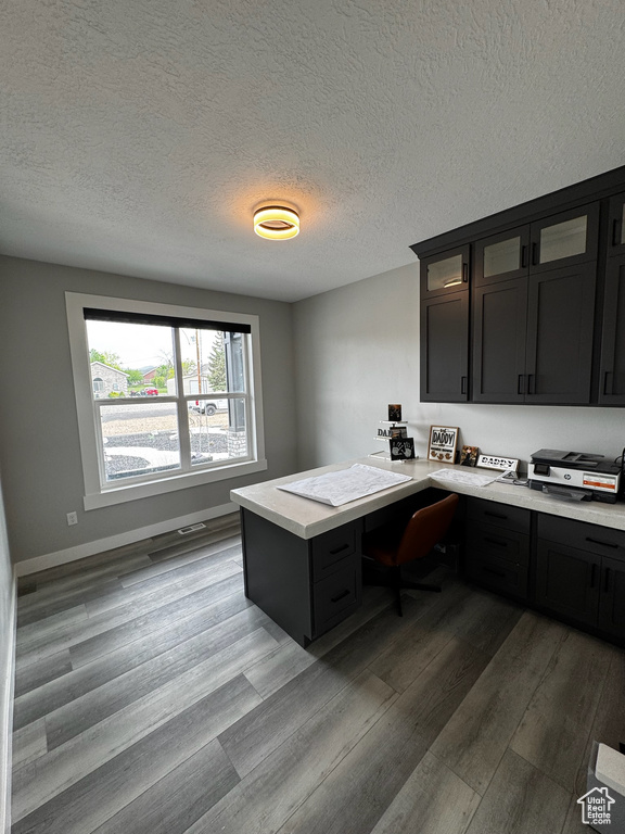 Office area with wood finished floors, built in desk, a textured ceiling, and baseboards