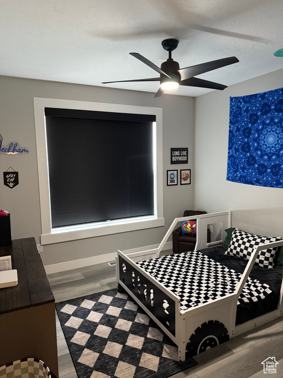 Bedroom with a textured ceiling, baseboards, ceiling fan, and wood finished floors