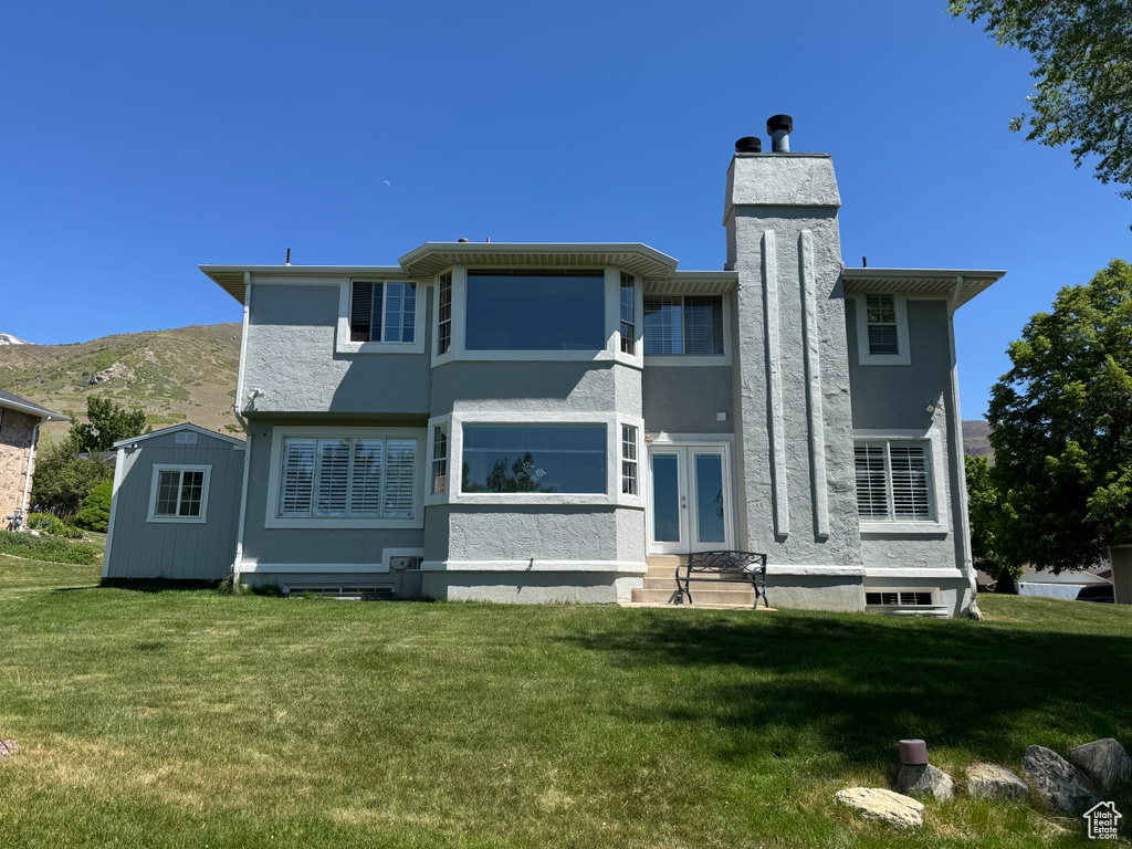 Rear view of property with a lawn, stucco siding, and french doors