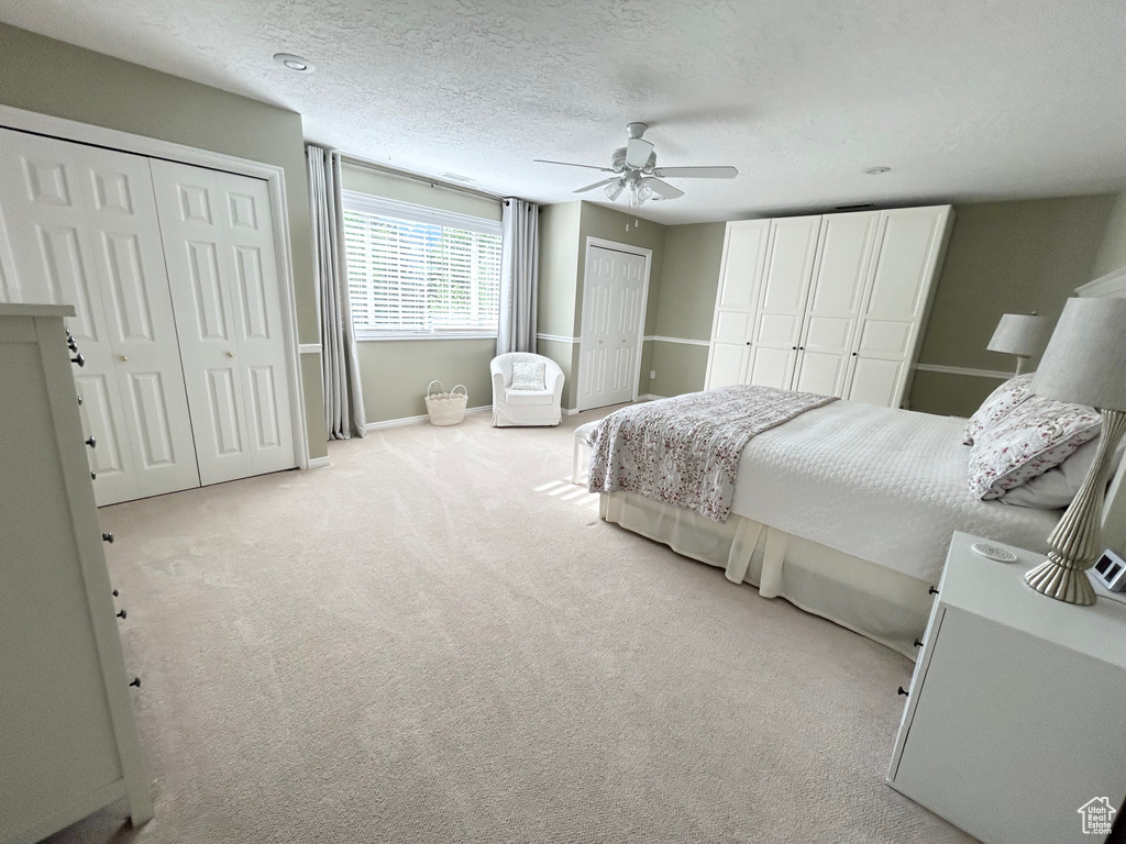 Carpeted bedroom featuring two closets, baseboards, and ceiling fan