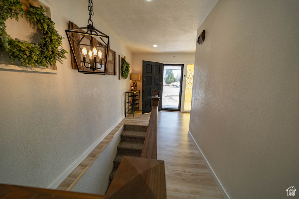 Hallway featuring light wood-style flooring, a chandelier, baseboards, stairs, and a textured wall
