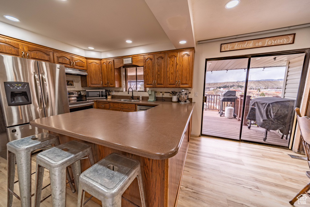 Kitchen with light wood-style flooring, brown cabinets, recessed lighting, appliances with stainless steel finishes, and a sink