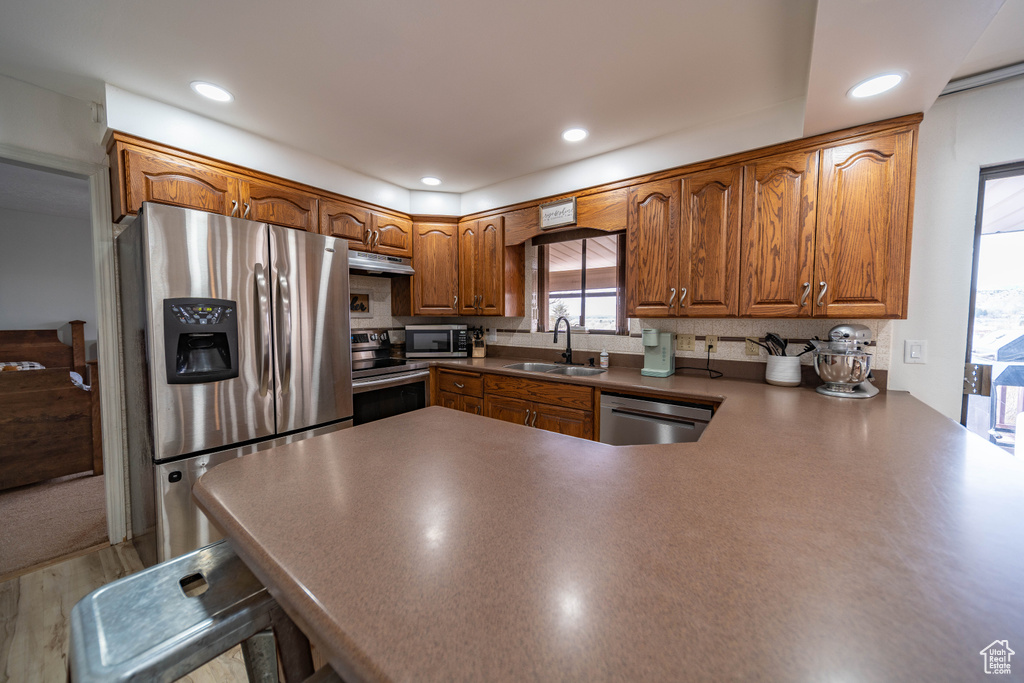 Kitchen with under cabinet range hood, a sink, a peninsula, appliances with stainless steel finishes, and brown cabinetry