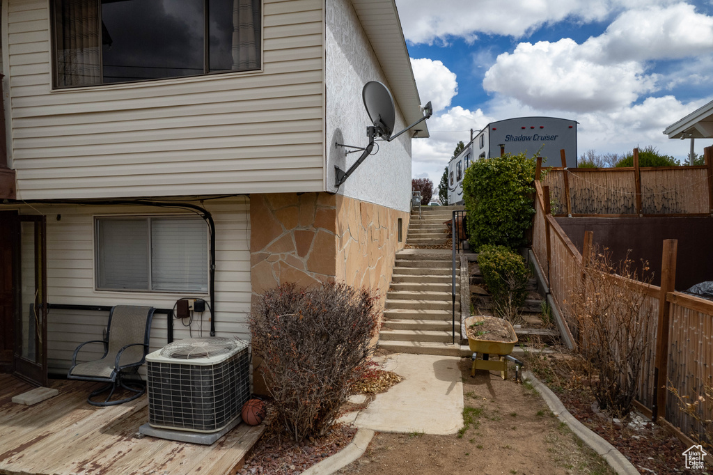View of home's exterior with stone siding, central air condition unit, fence, and stairway