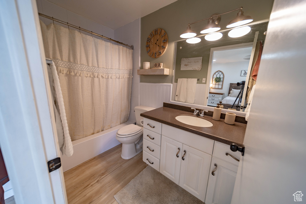 Ensuite bathroom featuring vanity, toilet, ensuite bath, shower / bath combo, and wood finished floors