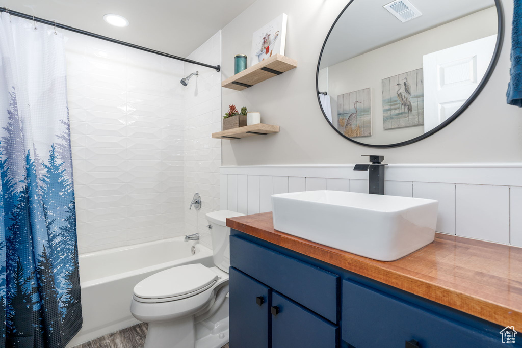 Full bathroom with vanity, toilet, a wainscoted wall, visible vents, and shower / bath combo with shower curtain
