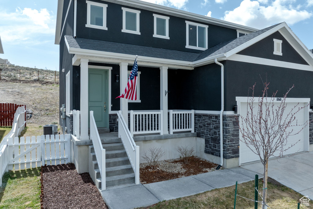 View of front of home with fence, roof with shingles, stone siding, covered porch, and a garage