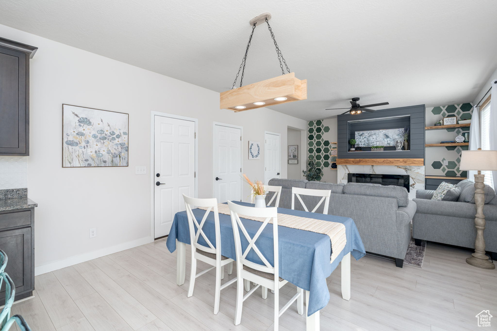 Dining area featuring baseboards, a fireplace, light wood-style floors, and ceiling fan