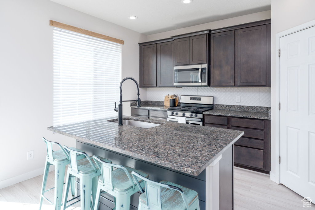 Kitchen with a kitchen bar, dark stone counters, a sink, dark brown cabinetry, and appliances with stainless steel finishes