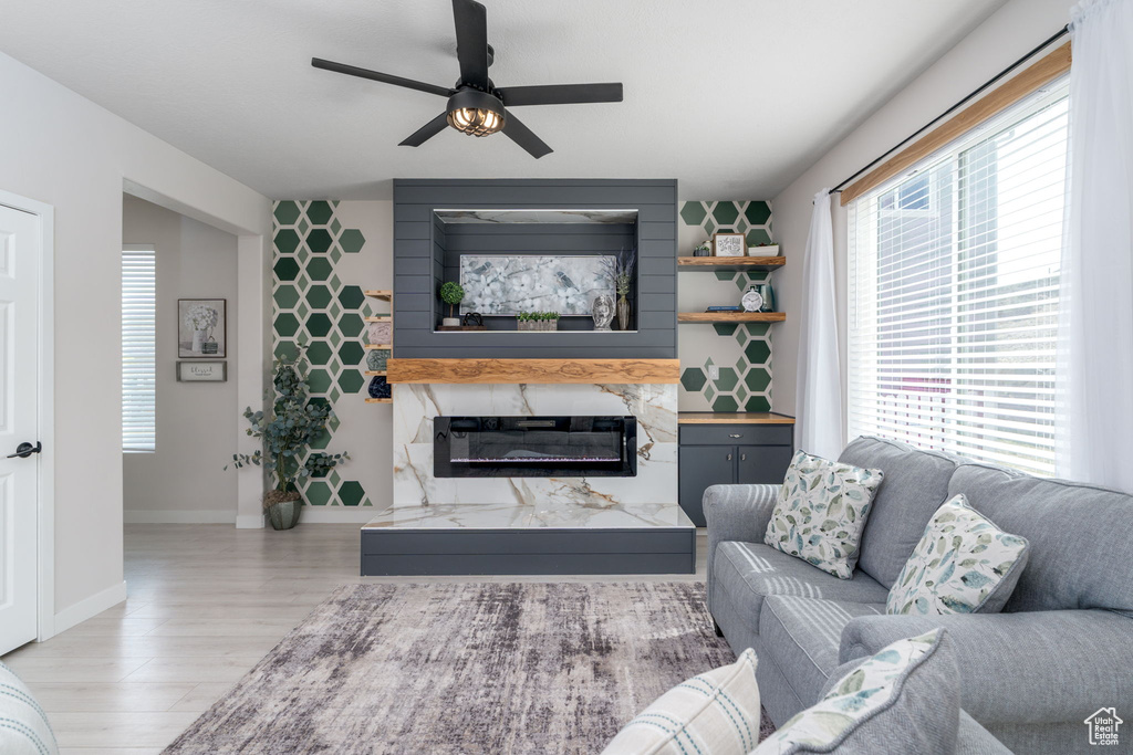 Living area with an accent wall, light wood-type flooring, a high end fireplace, baseboards, and ceiling fan