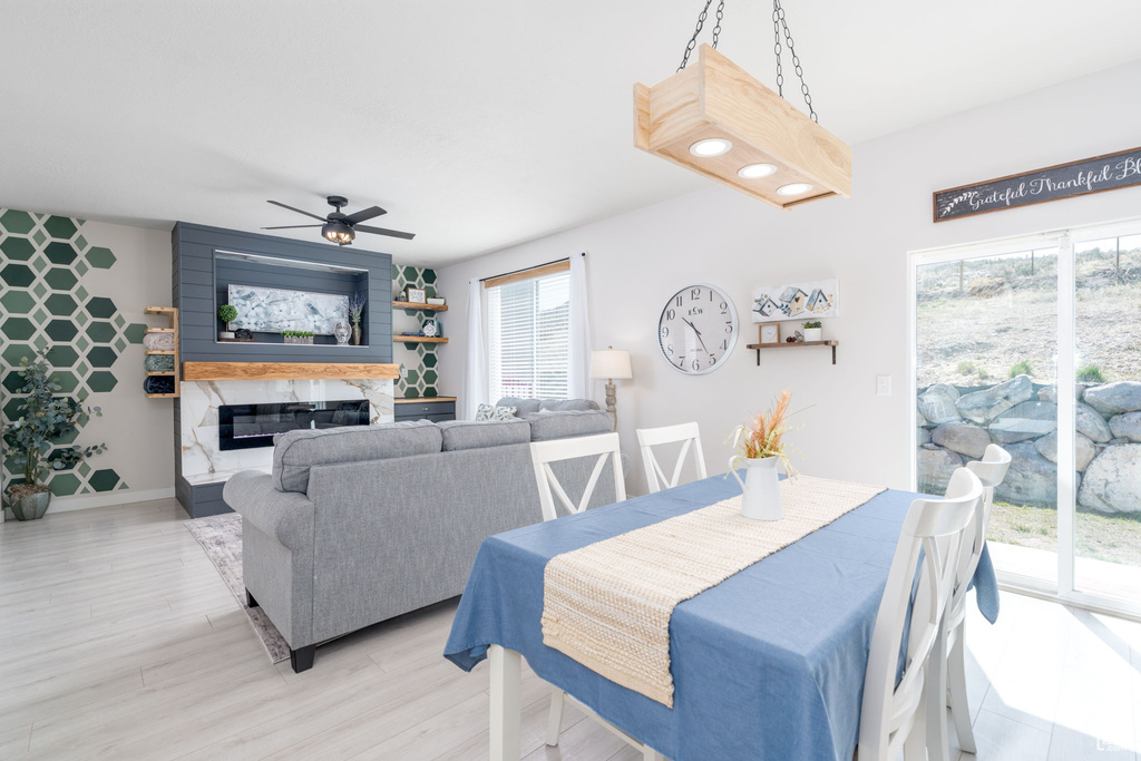 Dining space featuring a premium fireplace, baseboards, an accent wall, light wood finished floors, and a ceiling fan