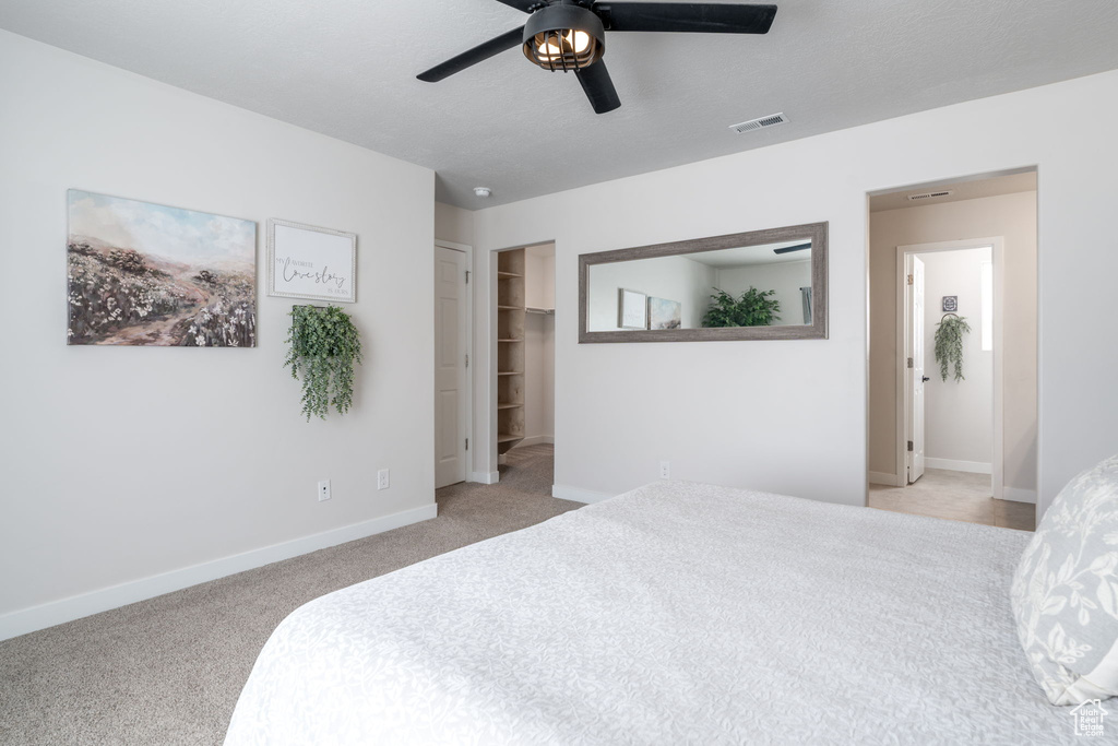 Bedroom featuring baseboards, visible vents, a walk in closet, and light carpet