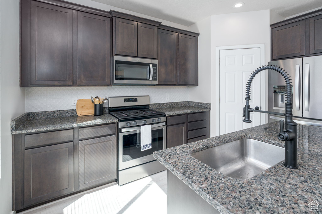 Kitchen featuring stainless steel appliances, decorative backsplash, dark stone counters, a sink, and dark brown cabinetry