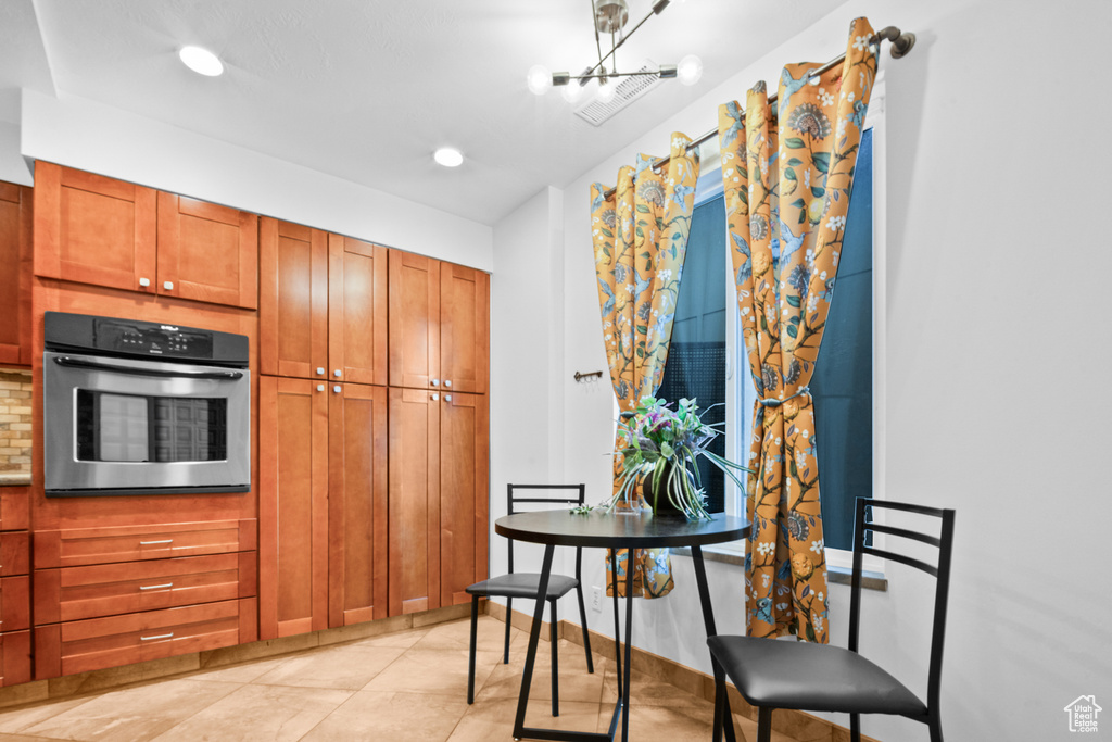 Kitchen featuring stainless steel oven, decorative backsplash, brown cabinetry, a chandelier, and recessed lighting