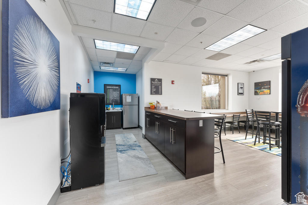 Kitchen featuring a breakfast bar, visible vents, a drop ceiling, and freestanding refrigerator