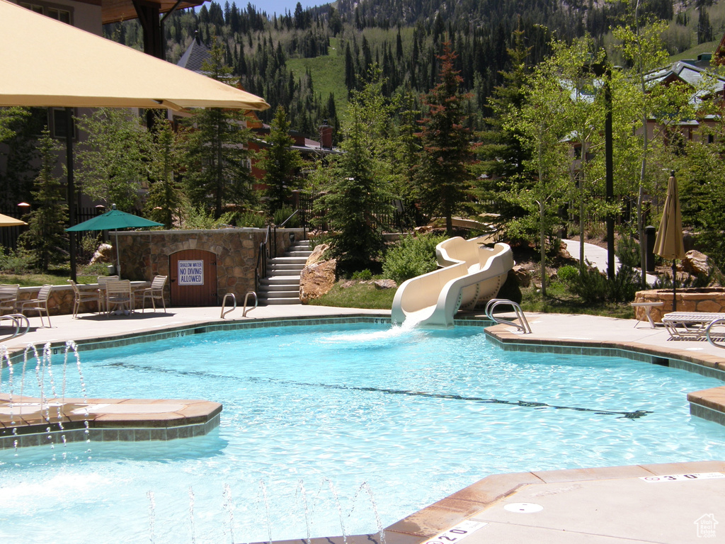 Community pool with a patio, stairs, a view of trees, and a water slide