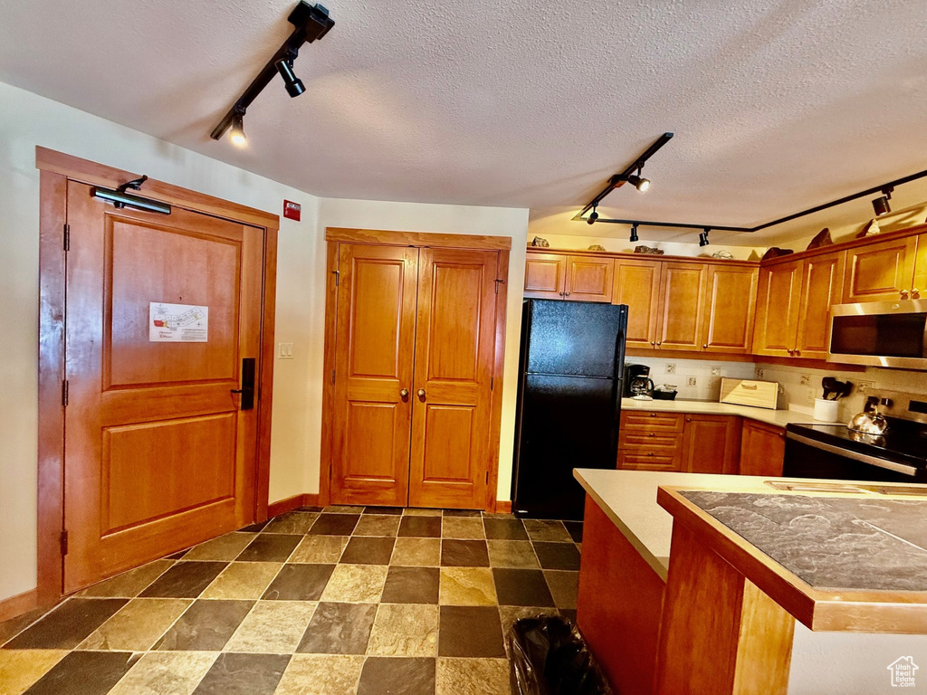 Kitchen with tile counters, appliances with stainless steel finishes, a textured ceiling, brown cabinets, and baseboards