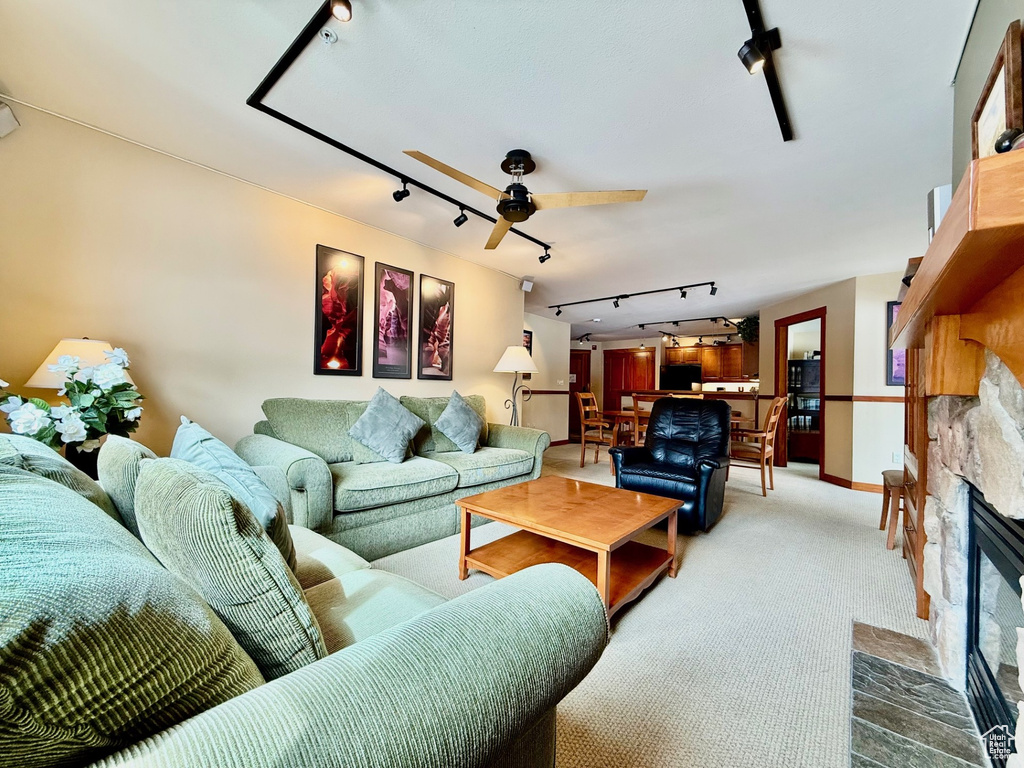 Living room featuring carpet flooring, rail lighting, a stone fireplace, and ceiling fan