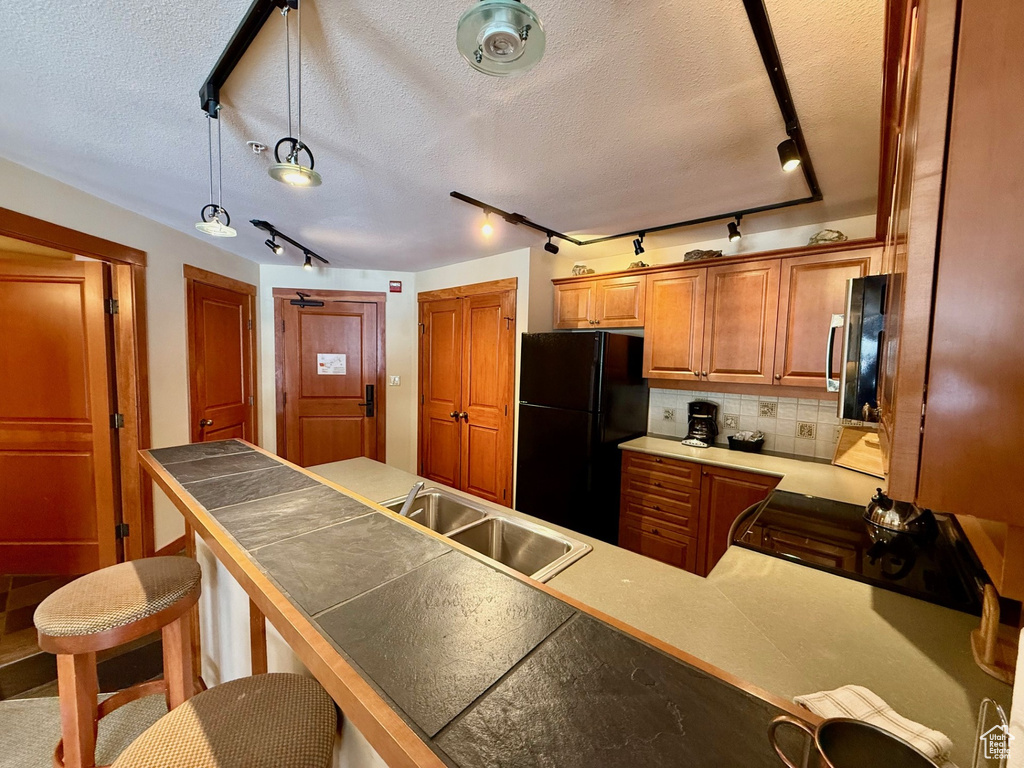 Kitchen featuring a sink, freestanding refrigerator, a kitchen breakfast bar, stainless steel microwave, and range with gas cooktop