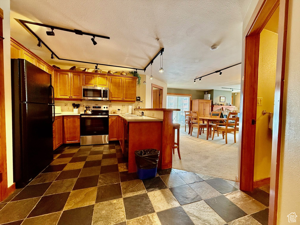 Kitchen featuring rail lighting, a peninsula, appliances with stainless steel finishes, and a textured ceiling