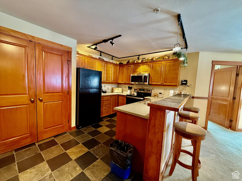 Kitchen featuring stainless steel appliances, a breakfast bar, a textured ceiling, a peninsula, and brown cabinets